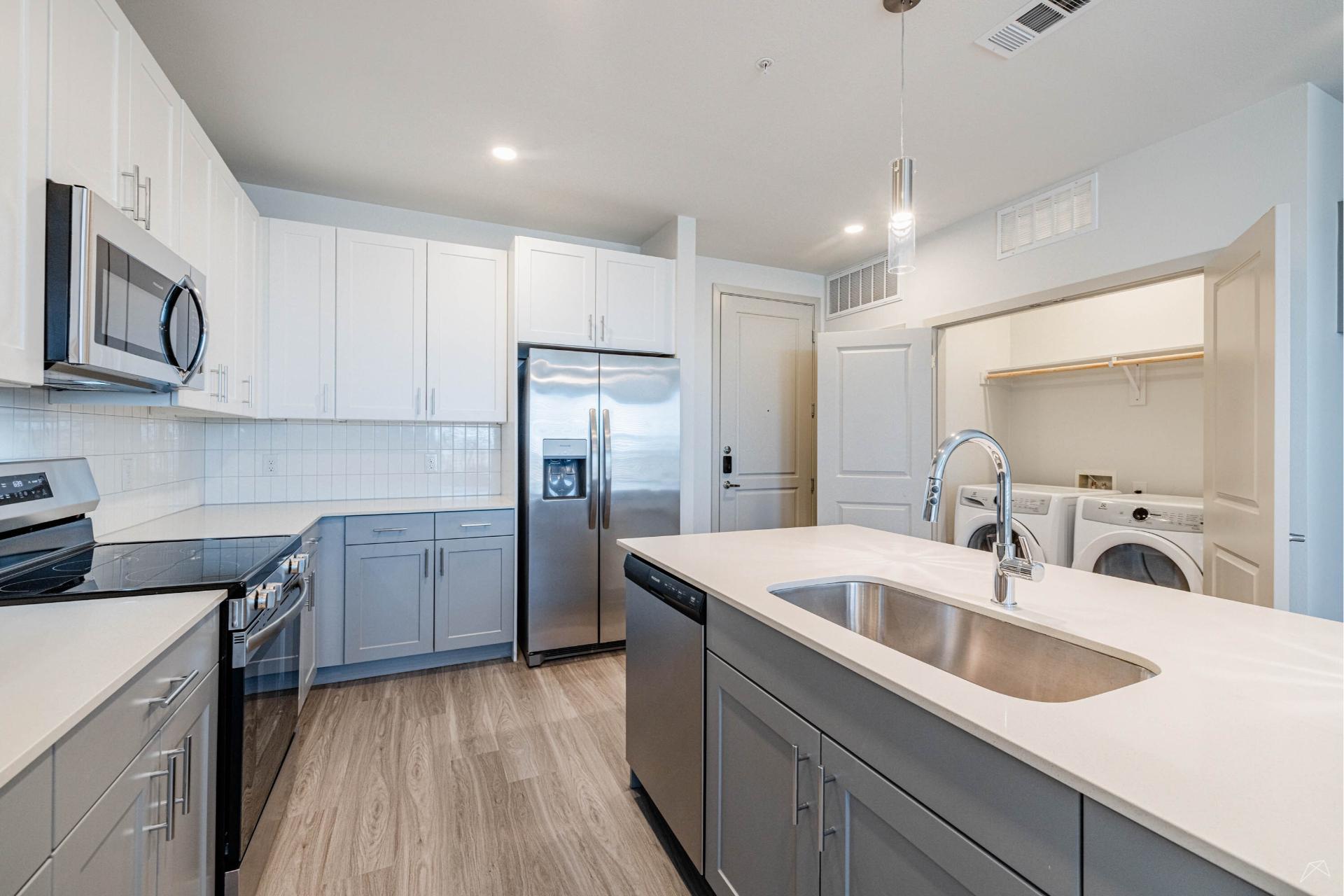 Modern kitchen with white and gray cabinets, stainless steel appliances, a wood-like island with sink, and laundry area in view.