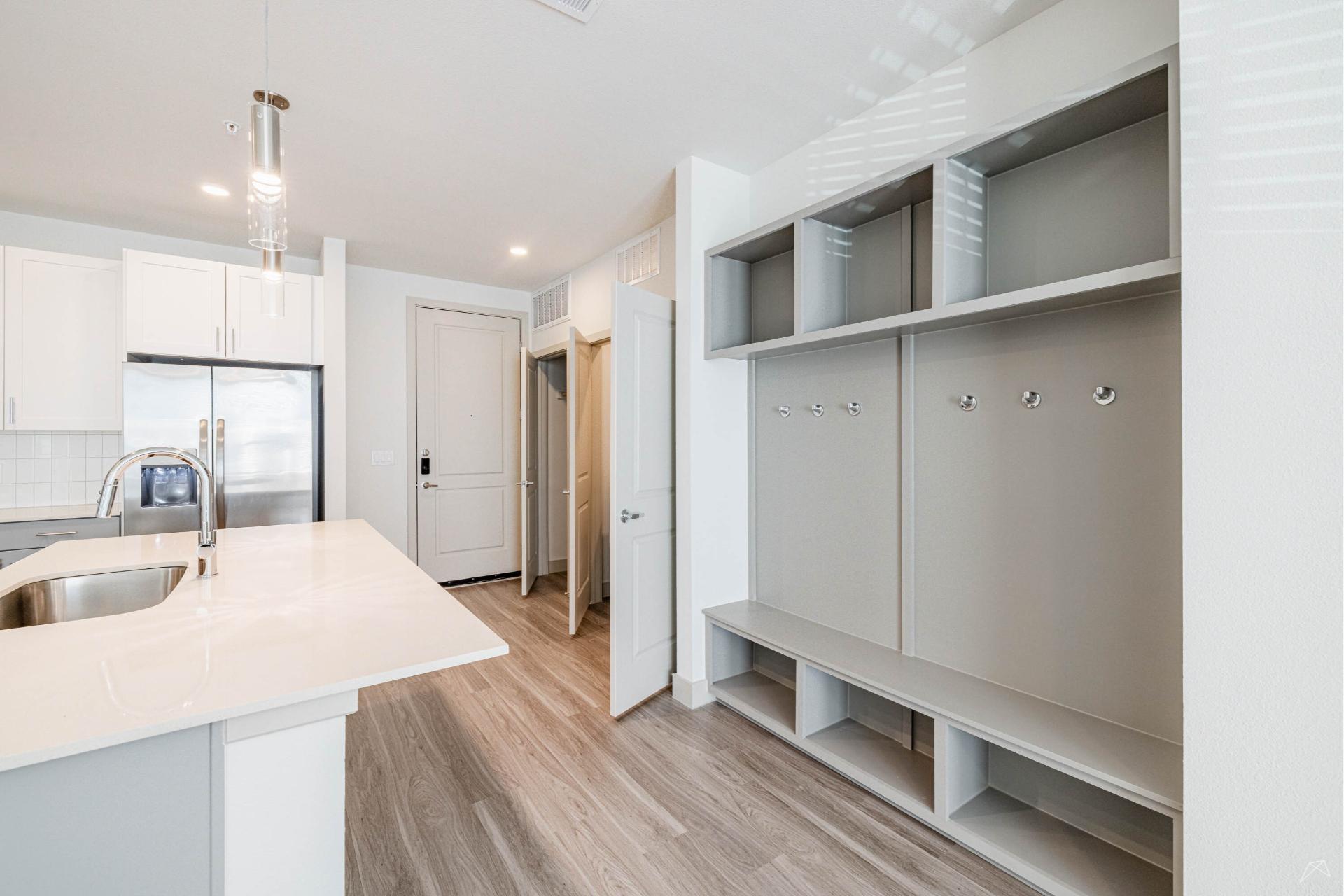 Modern kitchen with white cabinets, stainless fridge, quartz counters, built-in mudroom; light wood-look flooring throughout.