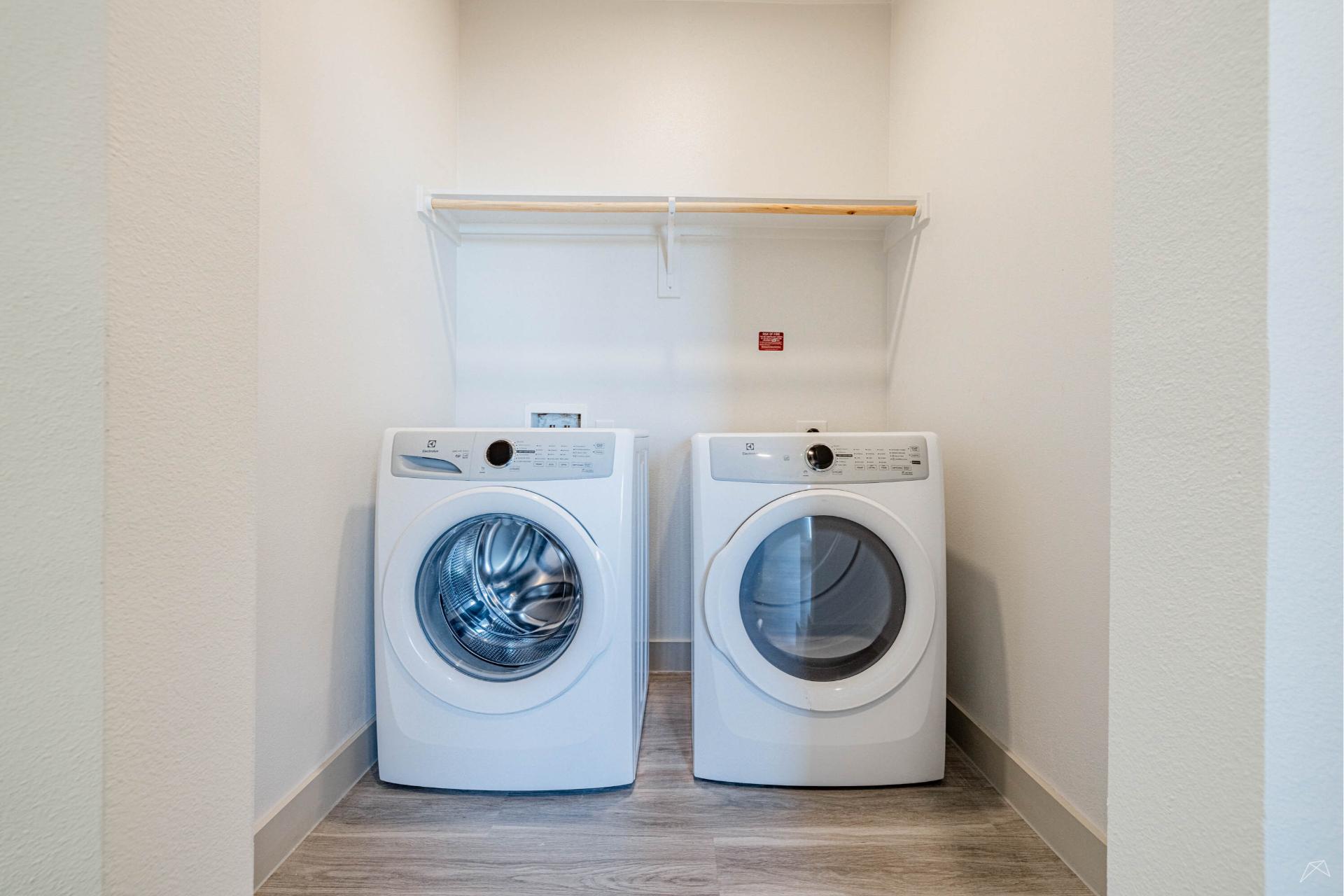A washing machine and dryer in a laundry room with wood-look cabinets and granite-style countertops.