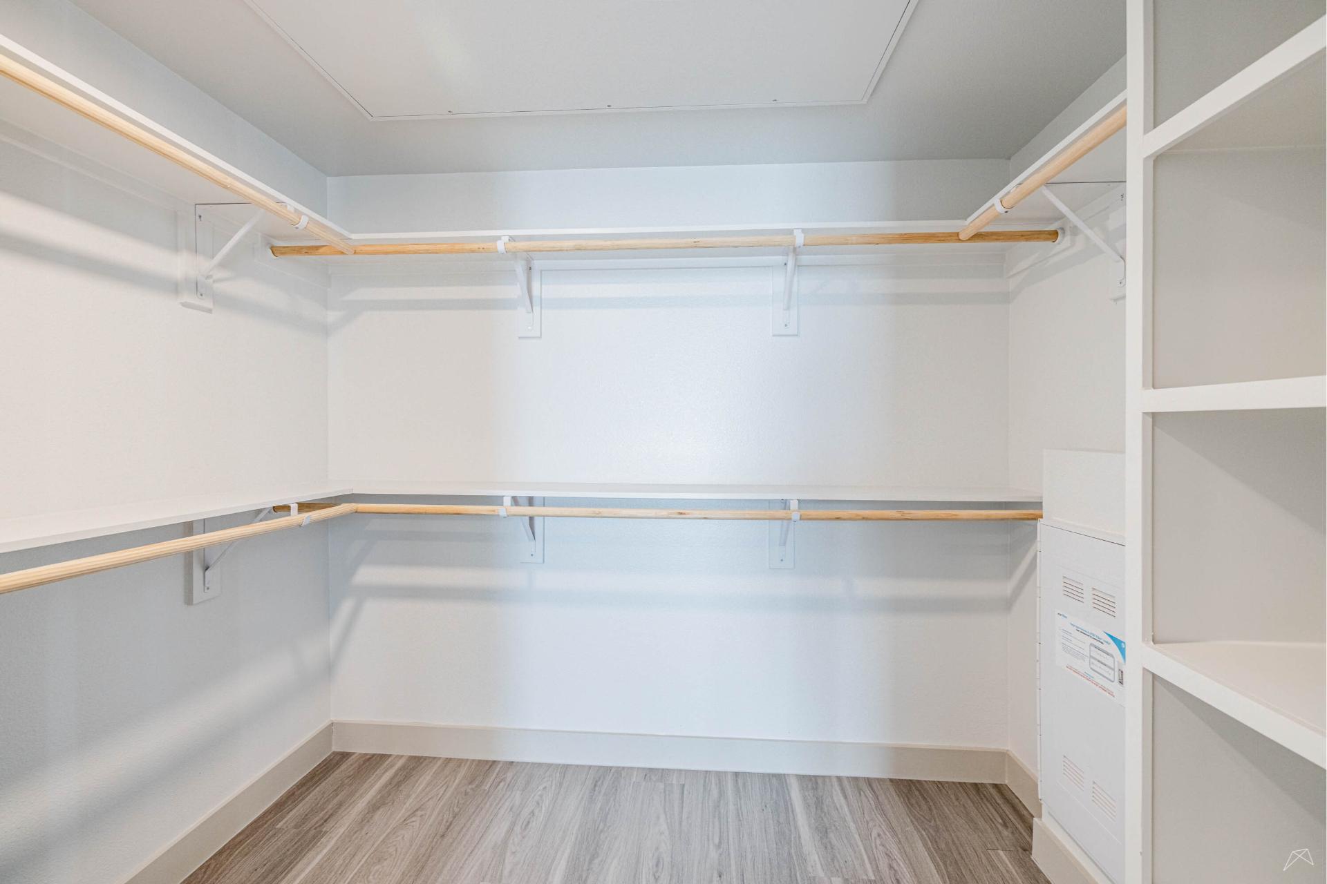 Spacious, empty walk-in closet with white walls, built-in shelves on the right, and hanging rods on two sides above light wood-look flooring.