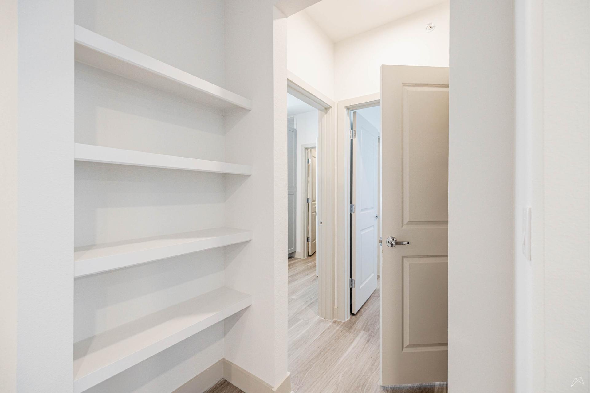 A small, bright hallway with built-in white shelves on the left, light wood-look flooring, and beige doors leading to other rooms.